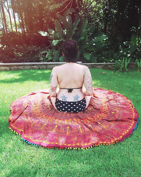 Mulher de biquini meditando de costas sob canga na grama